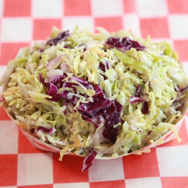Creamy coleslaw with green and purple cabbage in a paper boat on a checkered background.