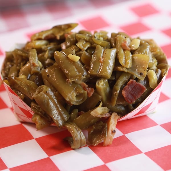 Green beans with bacon in a paper boat on a red and white checkered surface.