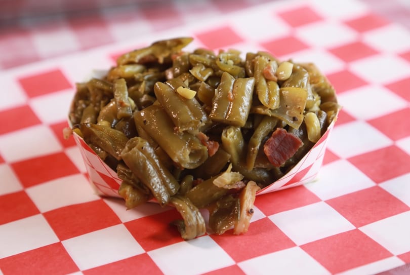 Green beans with bacon in a paper boat on a red and white checkered surface.