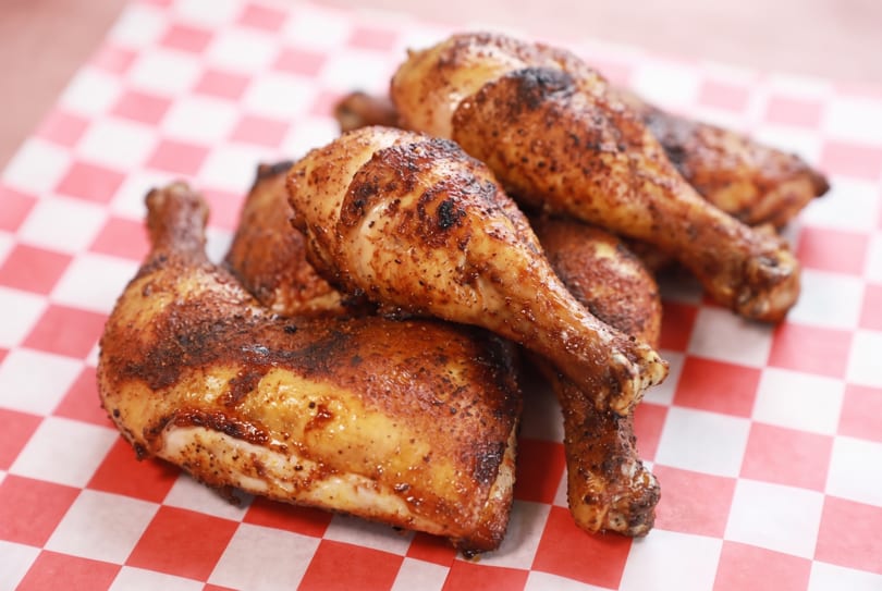 Golden-brown roasted chicken drumsticks and thighs on red and white checkered paper.