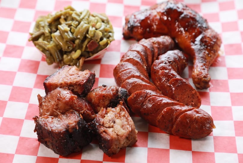 Barbecue platter with glazed chicken, sliced sausage, brisket burnt ends, and green beans.