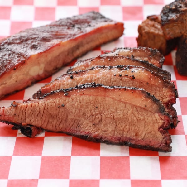 Barbecue platter with ribs, sliced brisket, and burnt ends on red and white checkered paper.
