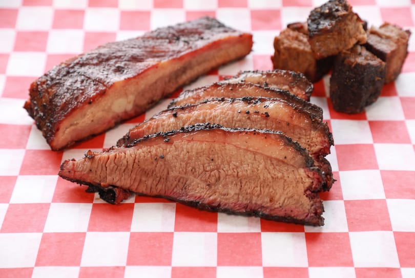 Barbecue platter with ribs, sliced brisket, and burnt ends on red and white checkered paper.